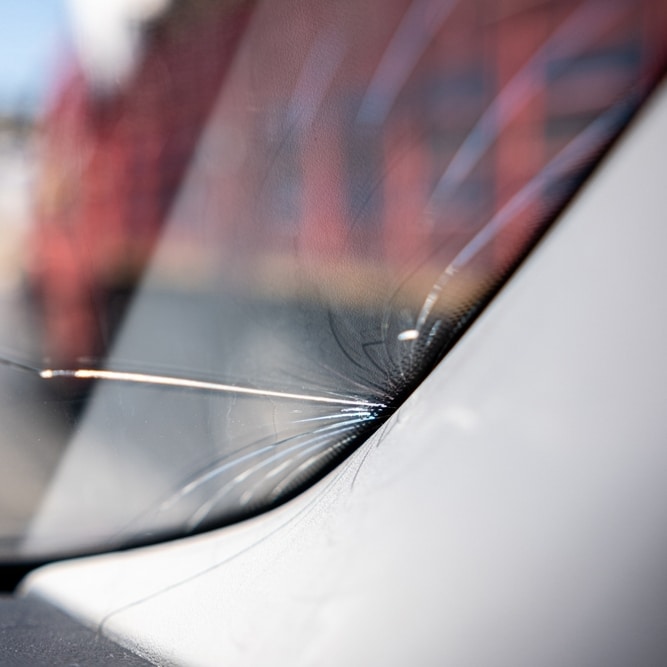 Fissure de pare-brise : quand réparer un bris de glace ? Gros plan d'une fissure en étoile sur le bas d'un pare-brise de voiture nécessitant une réparation de bris de glace.